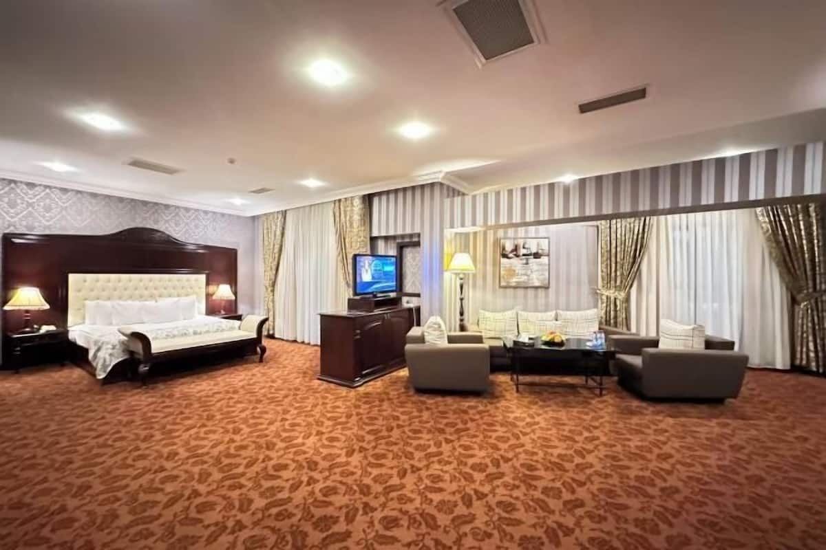 A hotel room with a large bed, a sofa, a TV, and a mirror.
