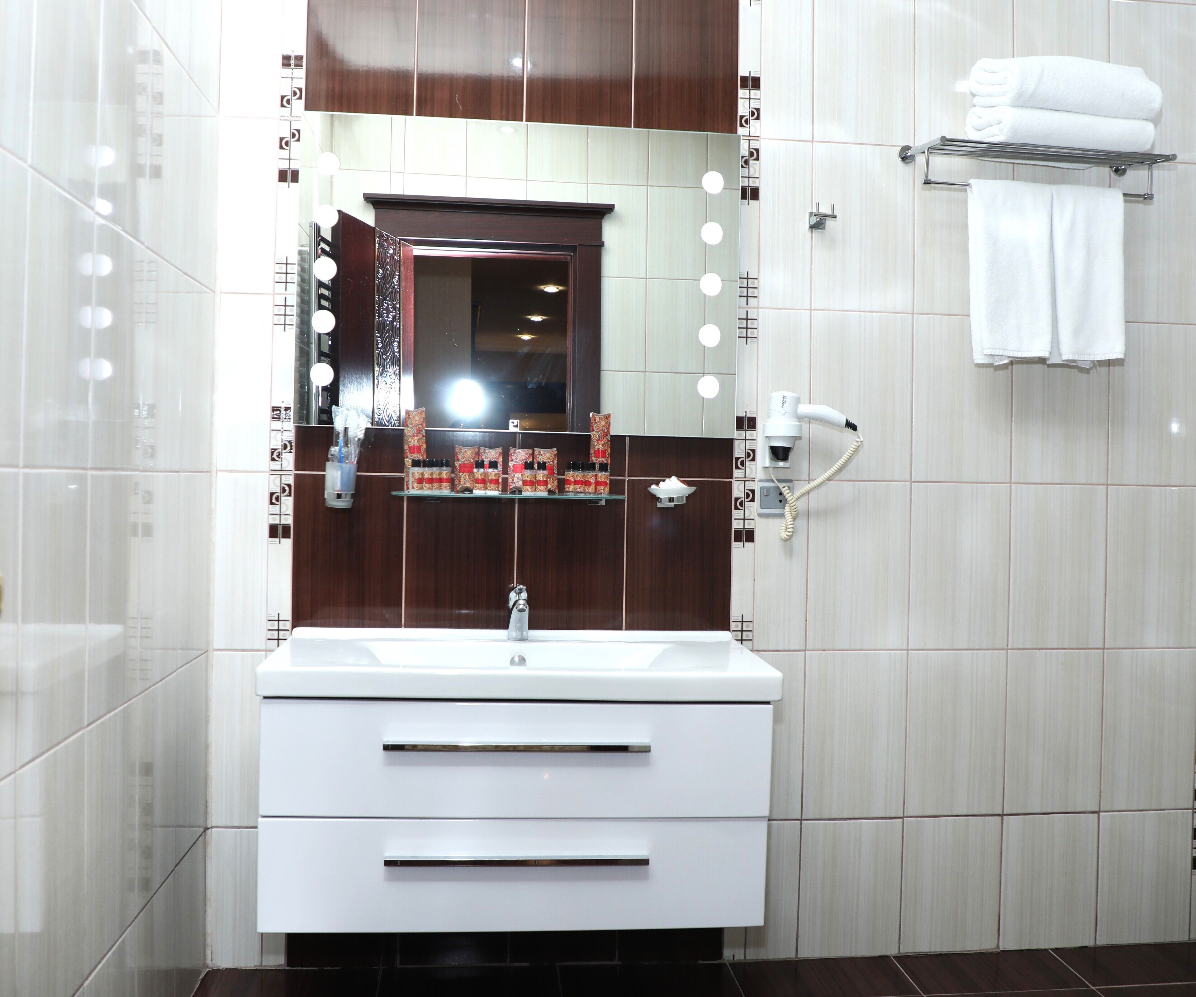 Un baño moderno con tocador, espejo con iluminación, secador de pelo y toallero.