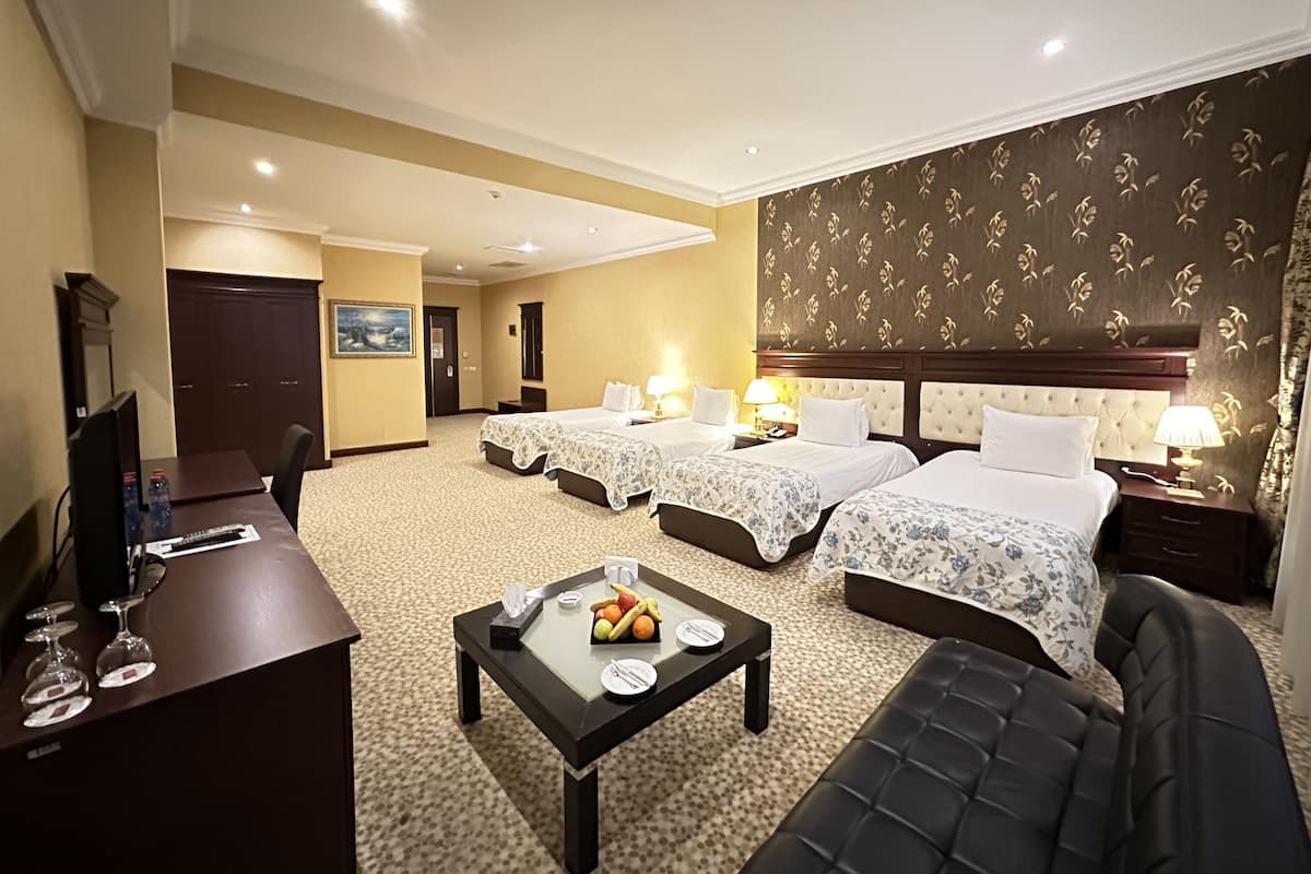 A hotel room with two beds, a desk, a chair, a coffee table with fruit, and a TV.