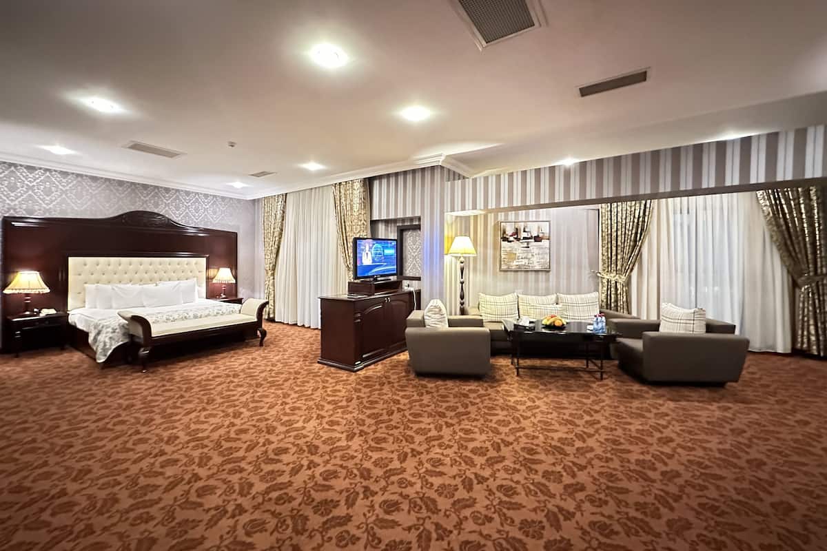 A hotel room with a large bed, a TV, a sofa, and a dining table.