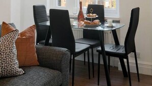 A dining area with a table and chairs, a window with blinds, and a sofa with cushions. - Chelsea Apartment | King`s Road, River Thames & Thames Clipper (London)