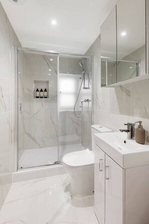 A modern bathroom with a glass-enclosed shower, a toilet, and a vanity with a mirror. - Chelsea Apartment | King`s Road, River Thames & Thames Clipper (London)