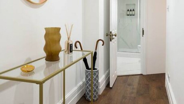 A hallway with a round mirror, a small table with a vase and candles, and a door leading to a bathroom. - Chelsea Apartment | King`s Road, River Thames & Thames Clipper (London)
