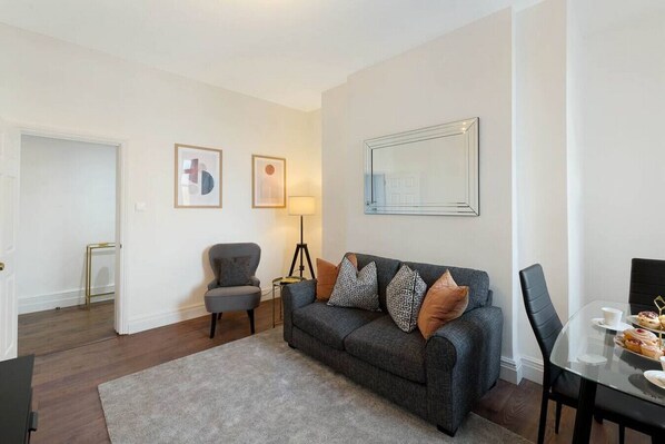 A modern living room with a grey sofa, a small side table, a floor lamp, and a dining table with chairs. - Chelsea Apartment | King`s Road, River Thames & Thames Clipper (London)
