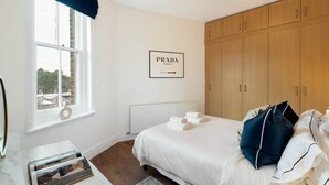 A bedroom with a bed, a window with a view, a wardrobe, and a framed sign on the wall. - Chelsea Apartment | King`s Road, River Thames & Thames Clipper (London)