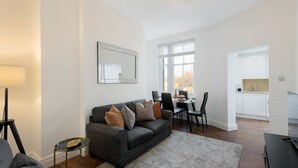 A modern living room with a grey sofa, a dining table with chairs, and a kitchen area visible through an open door. - Chelsea Apartment | King`s Road, River Thames & Thames Clipper (London)