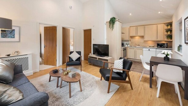 Eine moderne Wohnung mit Wohnzimmer, Essbereich und Küche. Es gibt einen Fernseher, ein Sofa und einen Esstisch.