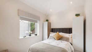 Ein Schlafzimmer mit Bett, Fenster mit Aussicht, Kleiderschrank und einem kleinen Tisch mit Pflanze.