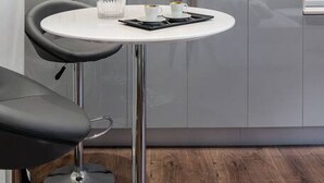 A modern kitchen with a built-in oven, a round dining table with two chairs, and a glass of water. - Chelsea Apartment | King`s Road, Sloane Sq, Lift & Underground Parking (London)