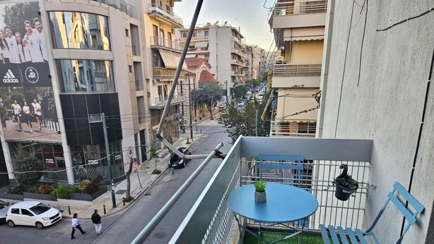 Un balcon avec une petite table et des chaises, donnant sur une rue animée par la circulation des voitures et des piétons.
