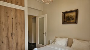 Une chambre à coucher avec un grand lit, une armoire en bois, un tableau accroché au mur et une porte donnant sur une autre pièce.
