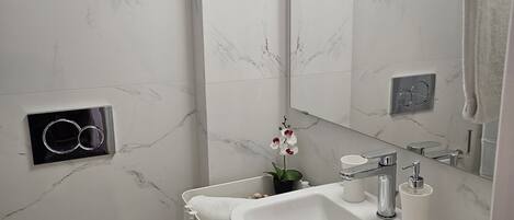 A modern bathroom with a white toilet, a sink with a mirror, and a shower area.