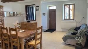 A dining area with a wooden table and chairs, a TV on the wall, and a window with a view of trees.