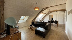 A loft-style room with a wooden ceiling, a black leather sofa, a small table, and a hanging light fixture.
