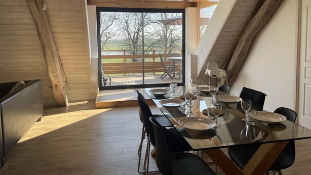 A dining area with a glass table and chairs, a wooden ceiling, and a view of the outdoors.