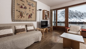 Ein gemütliches Wohnzimmer mit großem Fenster, einer Couch, einem Fernseher und einem Bücherregal.