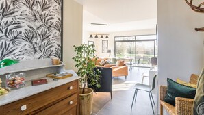 Una sala moderna con un gran cuadro abstracto en la pared, un mueble de madera, una planta verde y un sillón de mimbre.