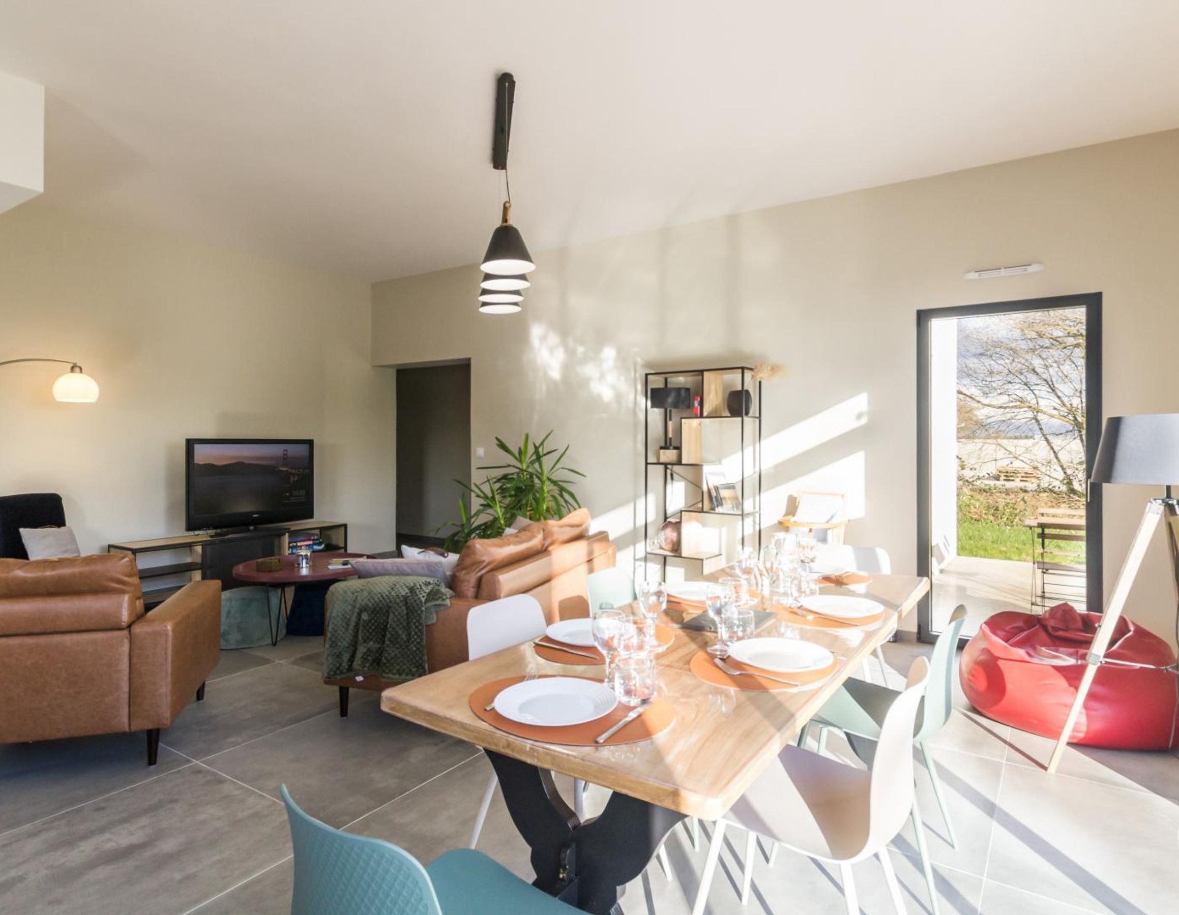 Una sala de estar moderna con comedor, televisor y un amplio ventanal con vistas al exterior.