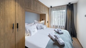 Une chambre d’hôtel avec une armoire en bois, un lit avec une literie et des oreillers blancs, une couvre-lit à motifs chevrons et une fenêtre avec des rideaux légers.