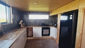 Et kompakt køkken med indbygget ovn, et sort køleskab og et vindue med naturligt lys.