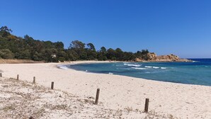 A beach with clear blue water, sandy shore, and a forested hill in the background. - Auberge de Cannedda (Sari-Solenzara)