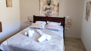 A neatly made bed with towels, a wooden headboard, and a large Buddha painting above it. - Auberge de Cannedda (Sari-Solenzara)
