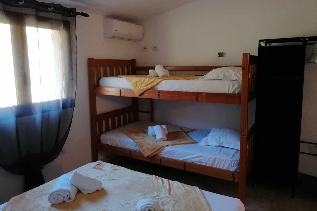 Une chambre avec un lit superposé, une fenêtre, des rideaux, un appareil de climatisation et un bureau avec une chaise.