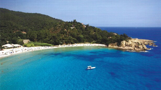 A coastal beach with clear blue waters, a boat, and a hilly backdrop. - Auberge de Cannedda (Sari-Solenzara)