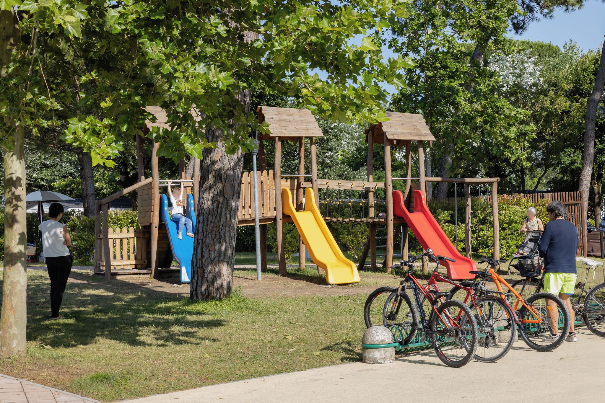 A playground with slides and climbing structures, surrounded by trees.