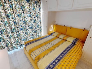 A bedroom with a yellow bedspread, floral curtains, and a white headboard.