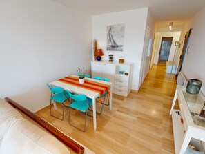 A modern dining area with a striped tablecloth, teal chairs, and a white cabinet with a sailboat painting above it.