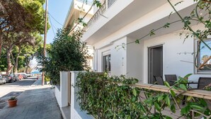 Ein modernes Gebäude mit weißer Fassade, einer überdachten Außenbereich-Sitzgelegenheit mit Stühlen und einem Blumentopf auf dem Bürgersteig.