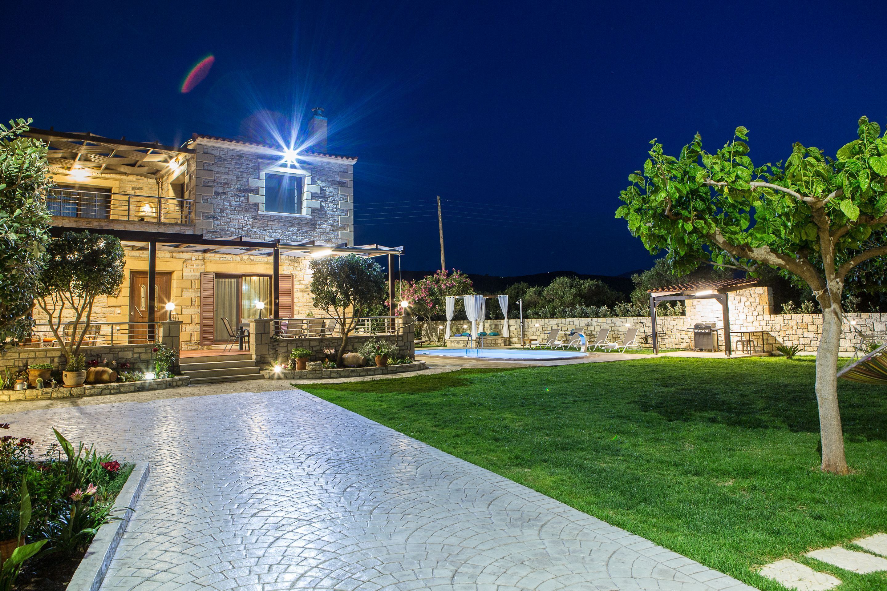 A two-story house with a stone facade, a swimming pool, and a well-maintained lawn.