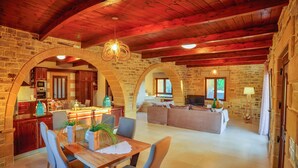 Un amplio salón con techo de madera, paredes de piedra, una mesa de comedor con sillas y un sofá.