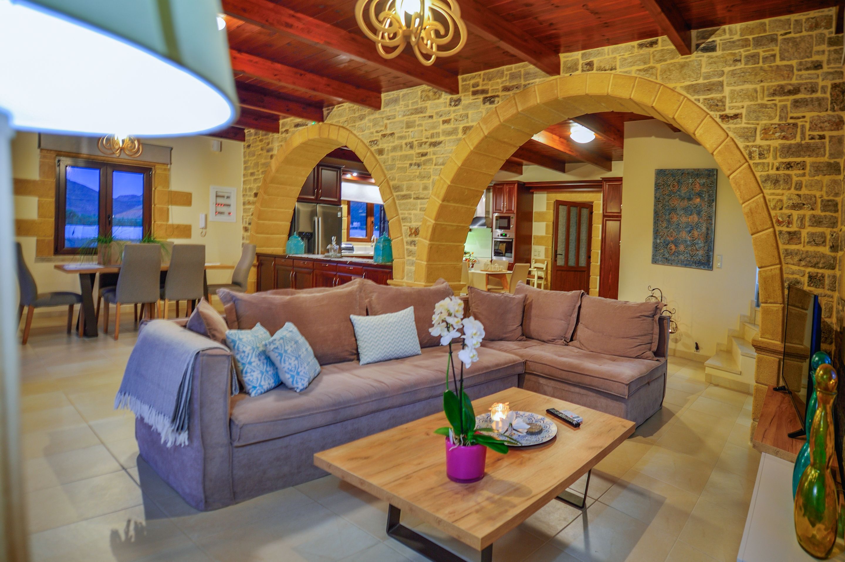 Uma sala de estar acolhedora com um sofá seccional, uma mesa de centro com um vaso de flores e uma cozinha visível através de um arco.