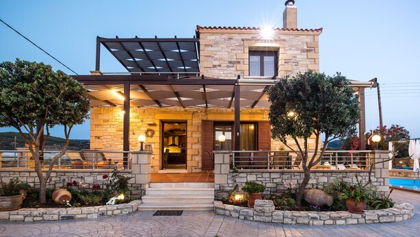 Una casa de piedra con porche cubierto, mobiliario exterior y piscina.
