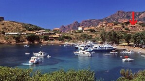 A coastal town with boats docked at a marina, a castle on a hill, and buildings along the hillside. - Spend exceptional holidays in a protected village , by the sea (Osani)