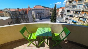 A balcony with a green table and chairs, overlooking a street with buildings and a clear sky. - Croparadise Hostel (Split)