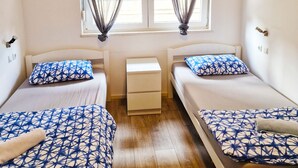 A room with two beds, a small bedside table, a window with curtains, and an air conditioning unit. - Croparadise Hostel (Split)