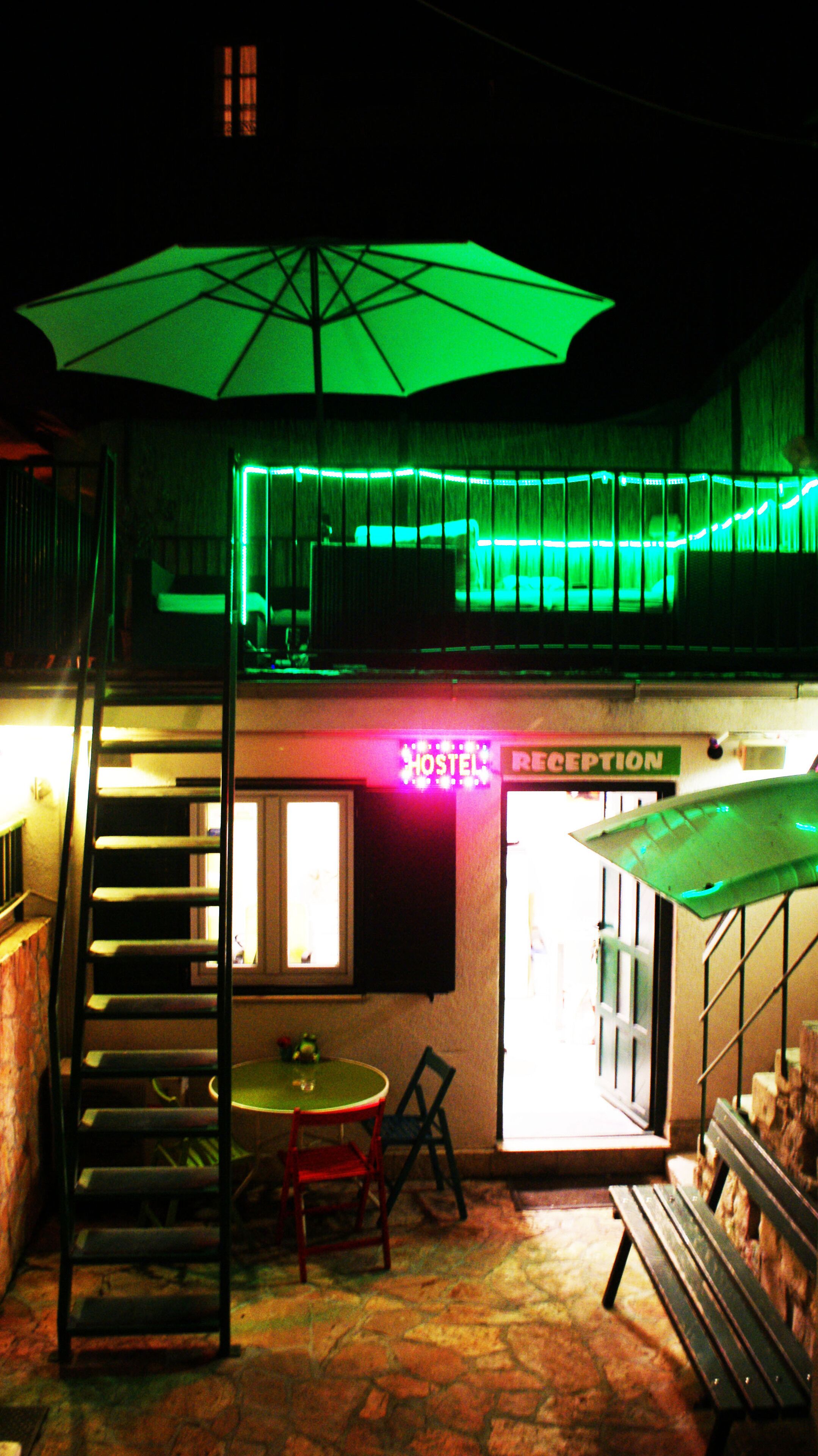 Un hall d’hôtel avec un escalier illuminé de lumière verte, un comptoir d’accueil et une table entourée de chaises.