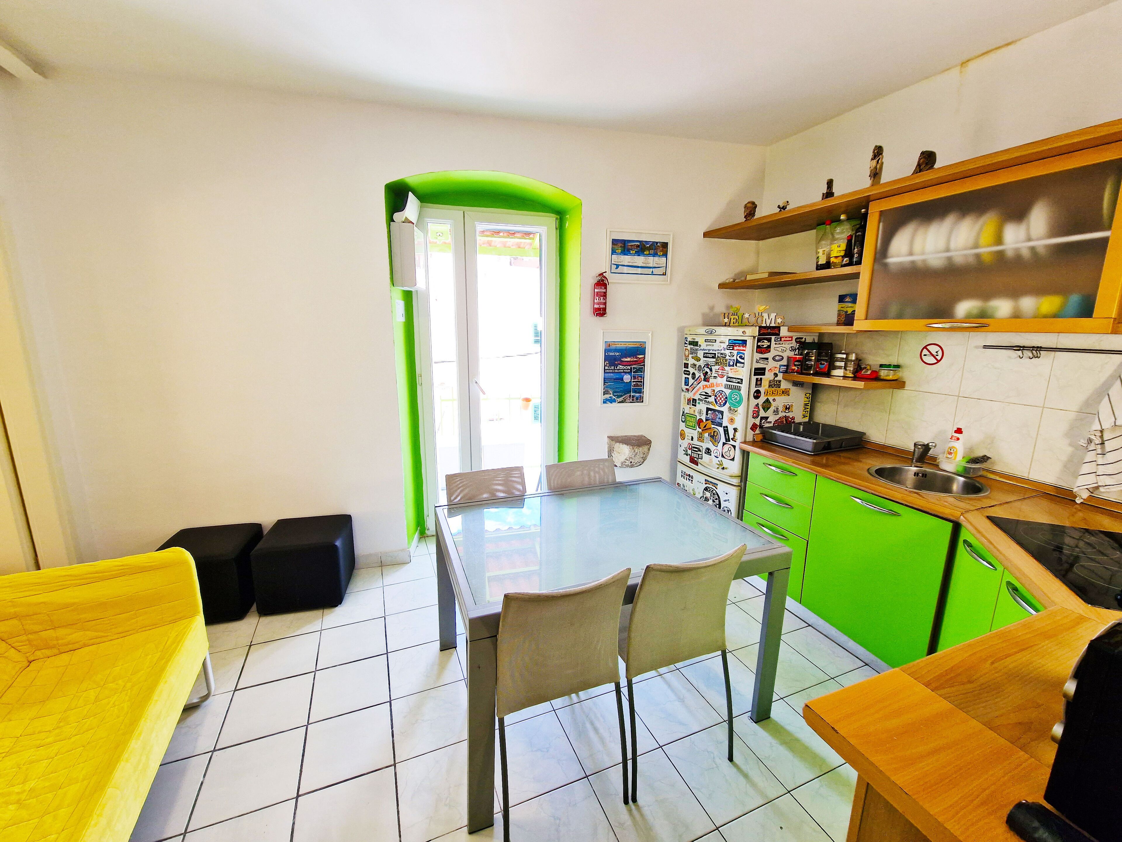 Une cuisine compacte avec un coin repas, des meubles de couleur verte et un réfrigérateur recouvert d’aimants.