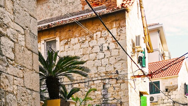 A narrow street with stone buildings, a potted plant, and a metal gate. - Croparadise Hostel (Split)