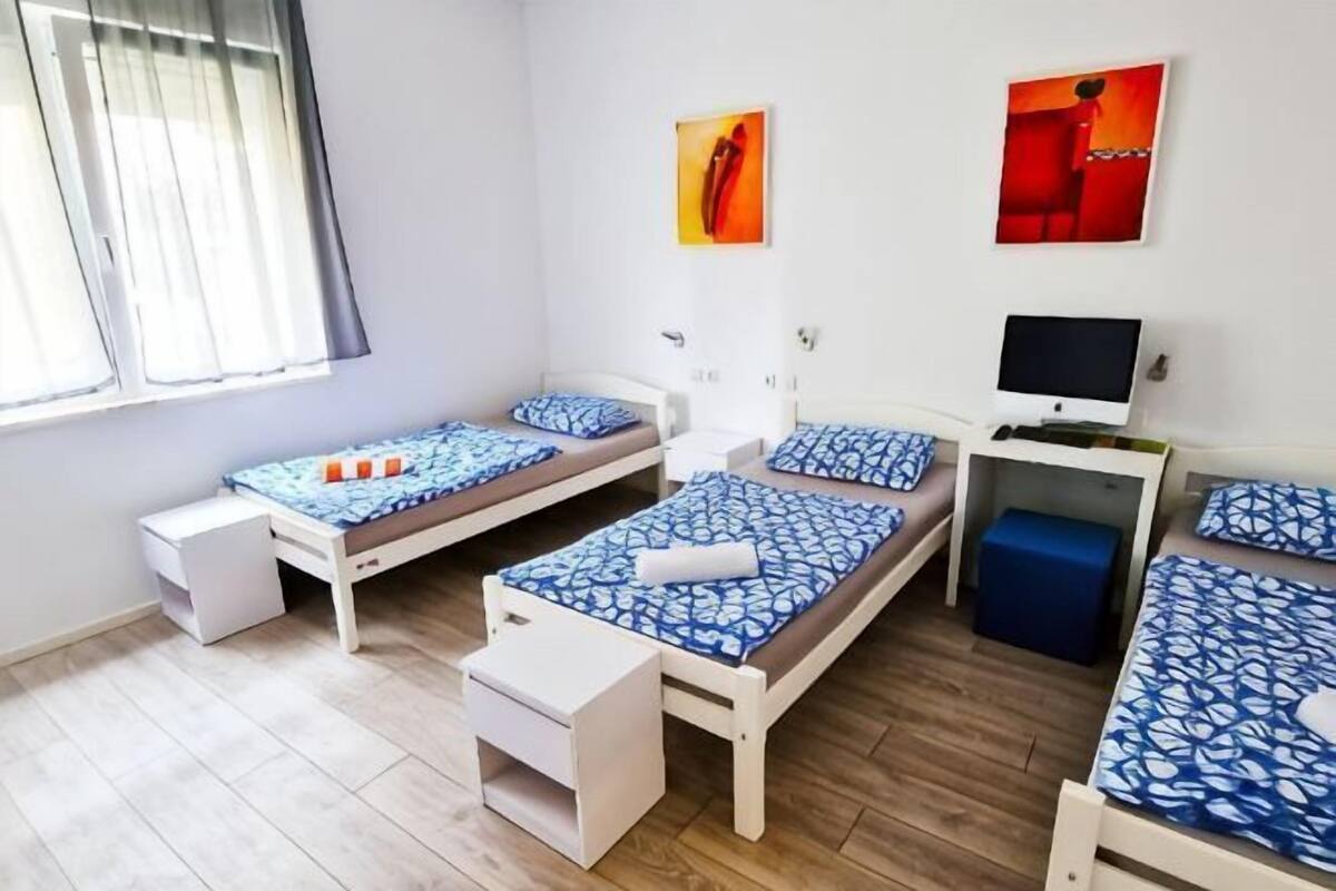 A room with three beds, a desk, a chair, and a window with curtains.