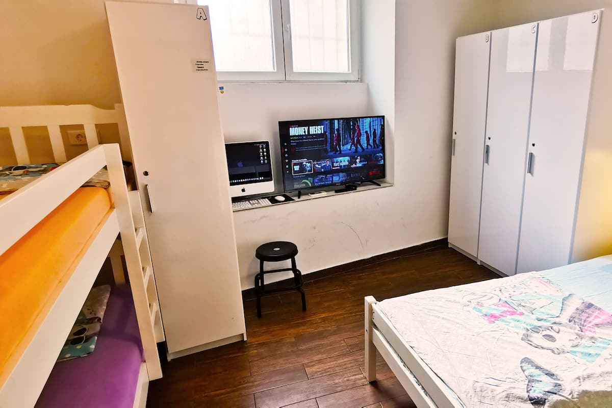 A bedroom with bunk beds, a desk with two monitors, a wardrobe, and a bedside lamp.