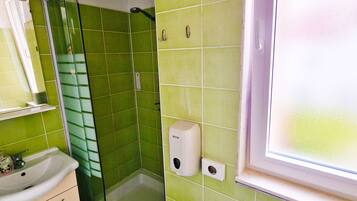 Casa de banho com azulejos verdes, uma pia, uma sanita e uma janela.