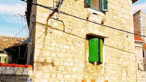 A stone building with a traditional design, featuring a small window with green shutters and a visible door. - Croparadise Hostel (Split)