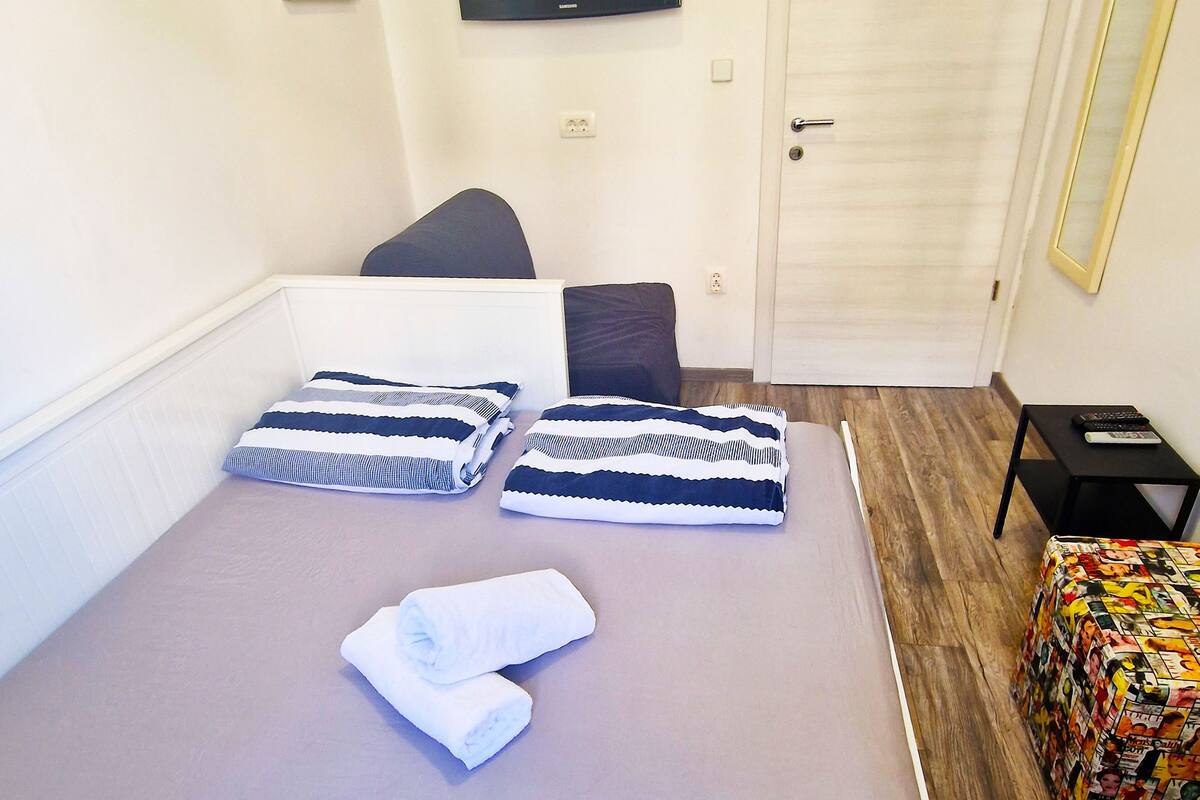 A neatly arranged bedroom with a bed, pillows, a TV, and a door.