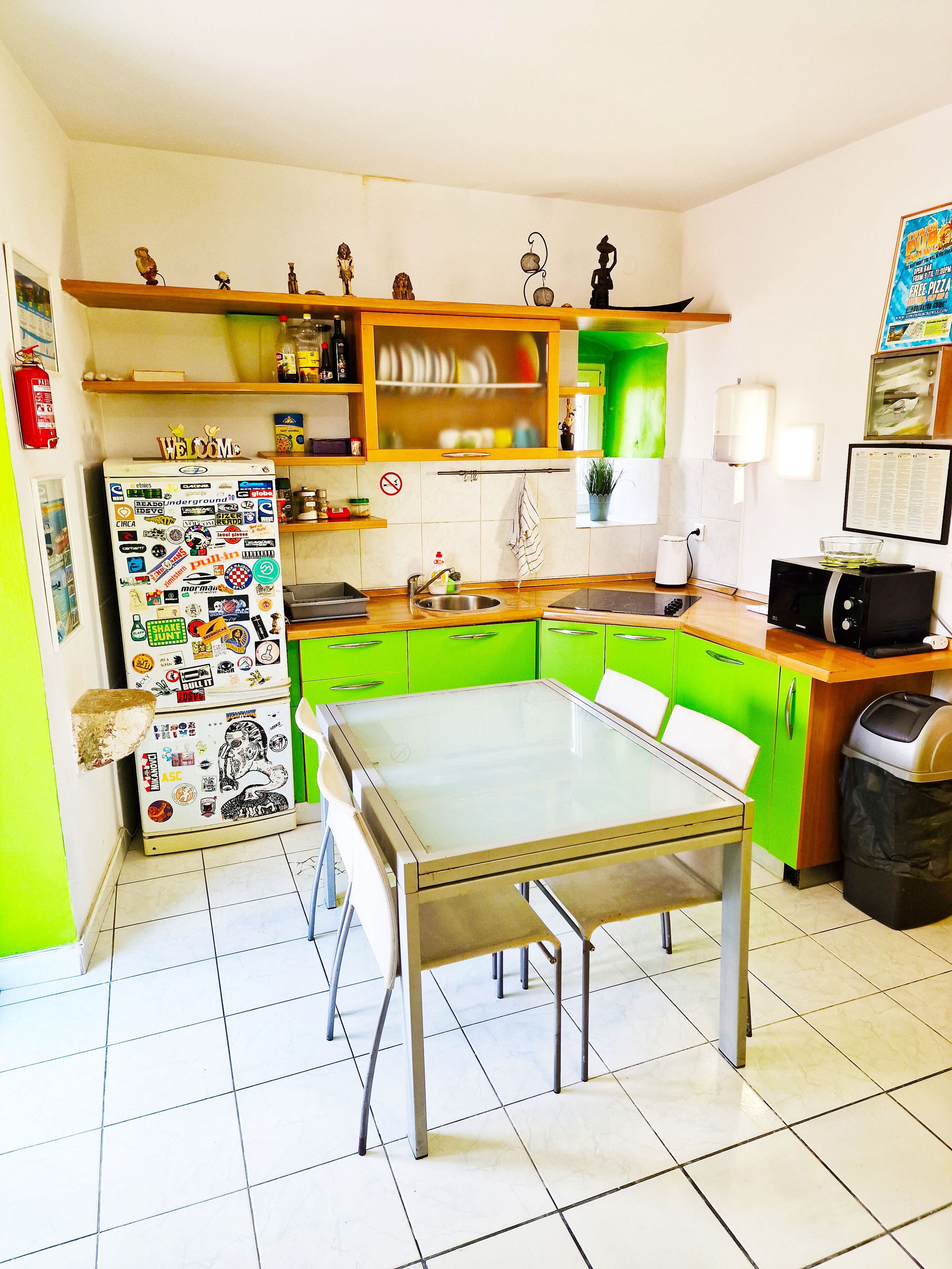 A compact kitchen with a dining table, green cabinets, and a refrigerator covered in stickers.