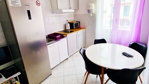 A compact kitchen with a refrigerator, microwave, and a small dining table with chairs. - Croparadise Hostel (Split)