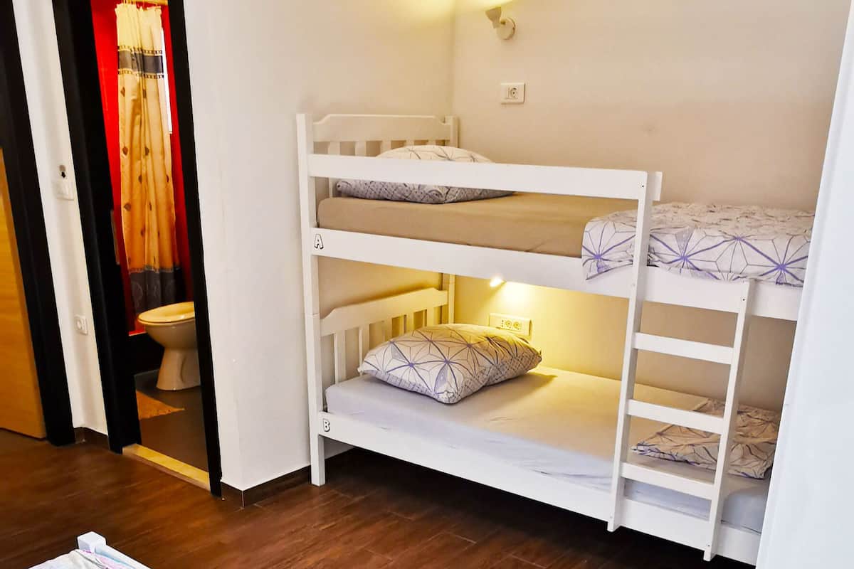 A room with a bunk bed, a small stool, and a wooden floor.